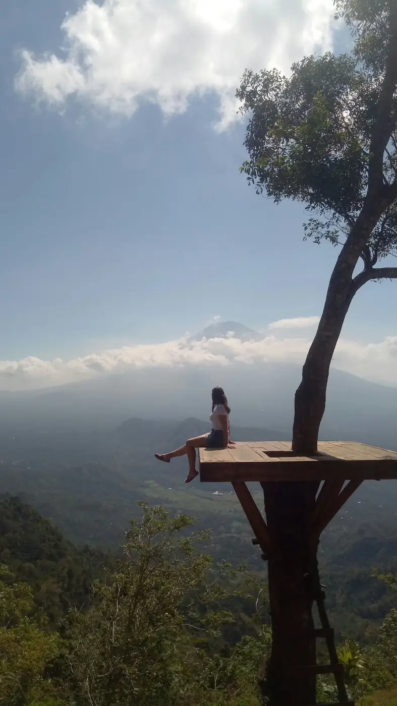 Visitor sitting on a wooden platform at Lahangan Sweet with Mount Agung behind