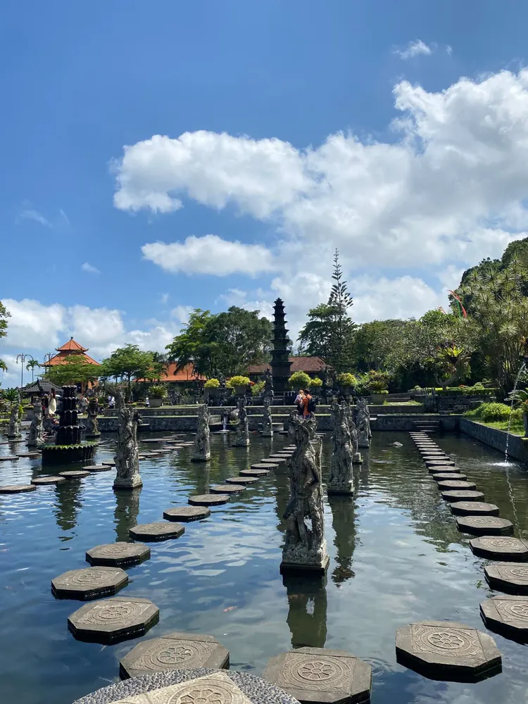 Stepping stones across the koi pond at Tirta Gangga Water Palace, with the tiered fountain behind