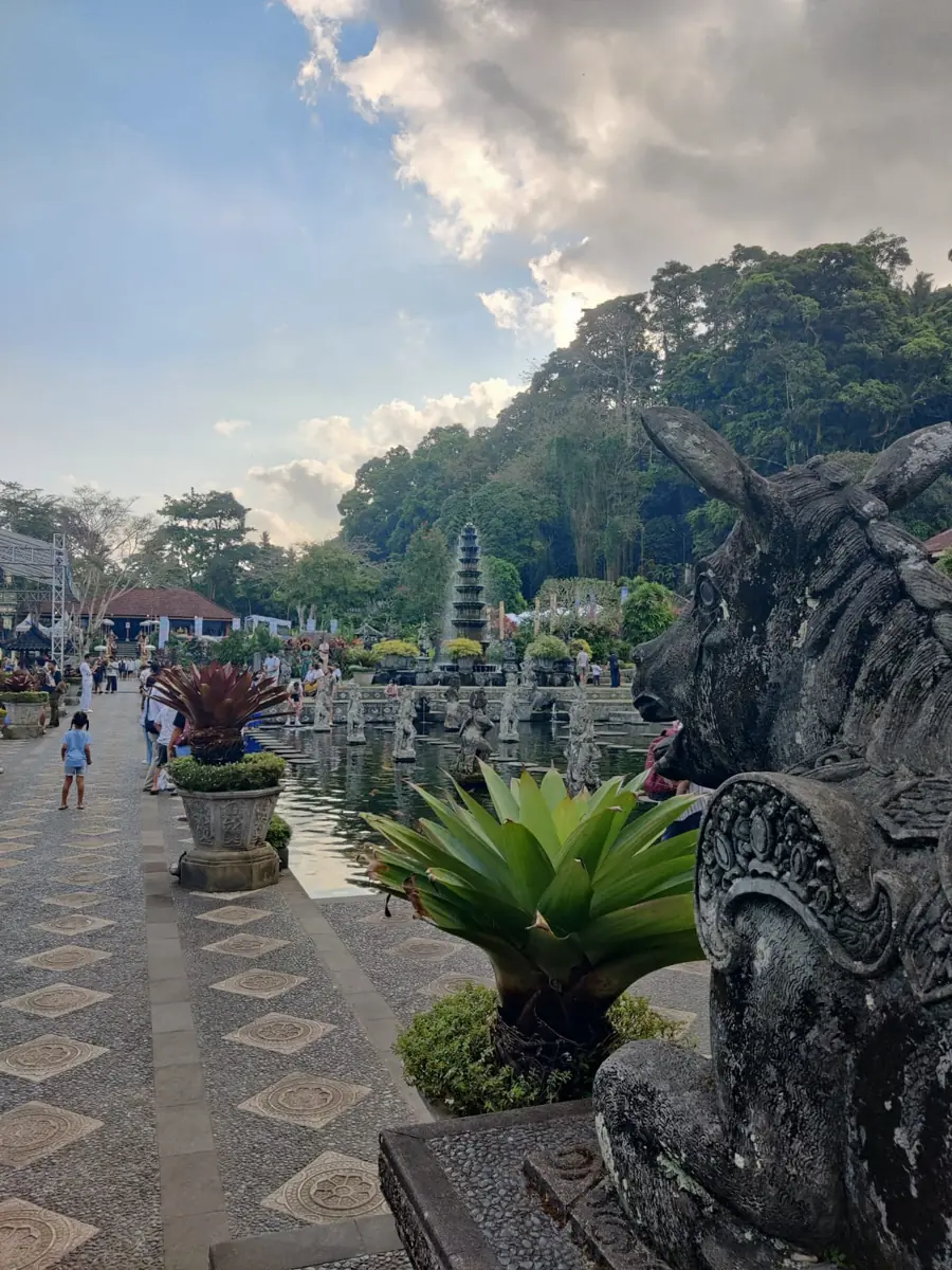 Carved bull statue beside the pond at Tirta Gangga, with the tiered fountain and forested hills behind
